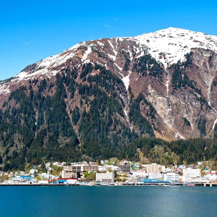 Juneau viewed from the water, nestled on the shore with towering mountains behind